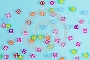 Multicolored plastic cube beads with letters scattered on blue background. Alphabet background texture