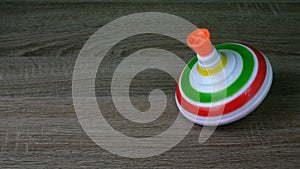 Multicolored plastic spinning top or whirligig top is traditional toy for preschool childs. Rotates in circle on wooden