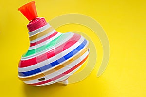 Multicolored plastic spinning top or whirligig top on yellow background. Toy for preschool childs. Children s school concept.