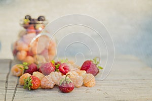 Multicolored raspberries in a glass jar with strawberries on background