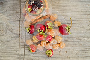 Multicolored raspberries in a glass jar with strawberries on background