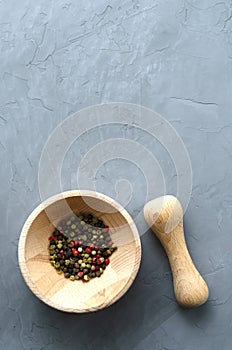 Multicolored red green black peppercorns in a wooden mortar with a pestle on a gray concrete background close-up with a