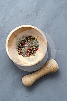 Multicolored red green black peppercorns in a wooden mortar with a pestle on a gray concrete background close-up with a