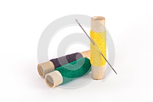 Multicolored sewing spools with threads and needle on white background