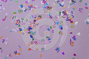 Multicolored sparkle glitter confetti letters on lilac for party or festive background. Holiday and fun concept