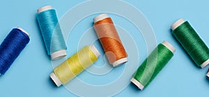 Multicolored spools of sewing threads on a blue background, top view