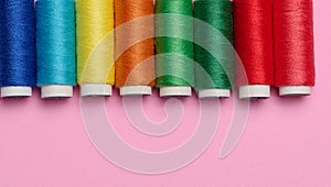 Multicolored spools of sewing threads on a pink background, top view