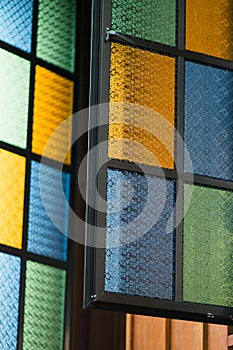 Multicolored stained glass window with rectangular pattern in blue, yellow and green attached to a traditonal Malay house