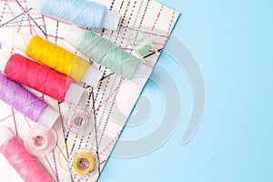 Multicolored thread coils and measuring tape on blue background. Sewing supplies, pattern and accessories for needlework,