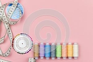 Multicolored threads of the coil, needle pins and centimeter on a pink background. Sewing supplies, patterns and