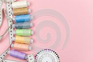 Multicolored threads of the coil, needle pins and centimeter on a pink background. Sewing supplies, patterns and