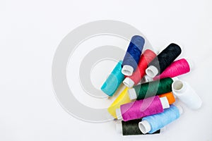 Multicolored threads for sewing on a white cotton fabric background.