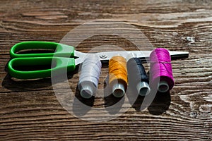 Multicolored threads and tailor scissors on wooden background