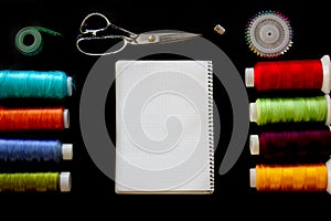 Multicolored threads, tape measure, scissors, pins and notepad for notes on a black background. View from above