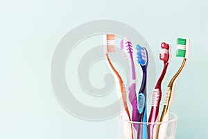 Multicolored toothbrushes in a glass cup, blue background