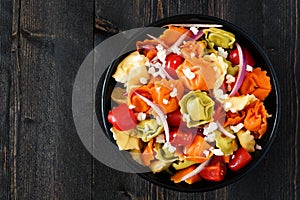Multicolored tortellini pasta salad, overhead view on dark wood