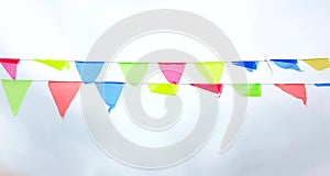 Multicolored triangular flags hang on a string and flutter in the wind against a cloudy cloudy sky
