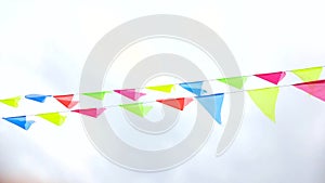 Multicolored triangular flags hang on a string and flutter in the wind against a cloudy cloudy sky