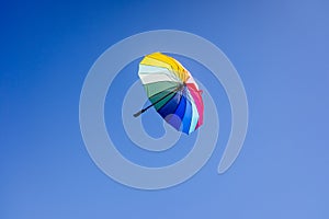 Multicolored umbrella flying suspended over bright blue sky background , with copy space