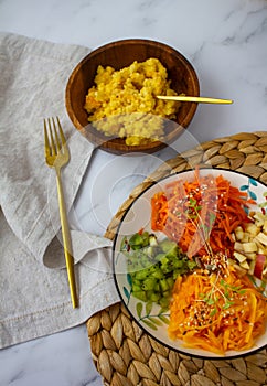 multicolored vegetable salad on a white plate and yellow millet porridge in a wooden bowl vertically