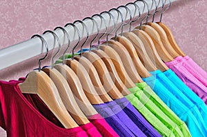 Multicolored women's t-shirts hanging on wooden hangers.