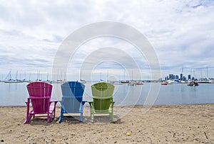 Multicoloured Muskoka Cottage chairs on the sand the beach looking out to the harbor and downtown Etobicoke in the background