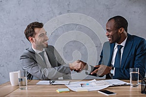 Multicultural business partners shaking hands at working table