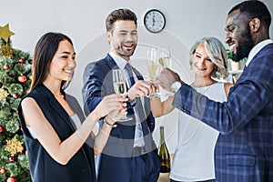 multicultural businesspeople clinking with glasses of champagne with christmas tree on background