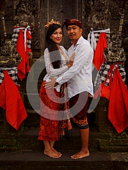 Multicultural couple standing near the temple in Bali. Caucasian wife and Balinese husband wearing traditional clothes. Culture