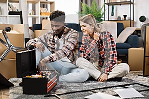 Multicultural couple with toolbox sitting at new home