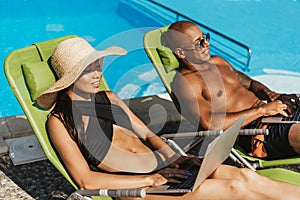 multicultural couple using laptops while relaxing on sunbeds