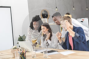 multicultural excited business people looking at laptop screen together at workplace