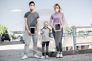 multicultural family with child in protective masks holding tablets air