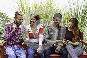 Multicultural friends having fun together looking at their smartphones  at dehor garden on college campus - People addicted by