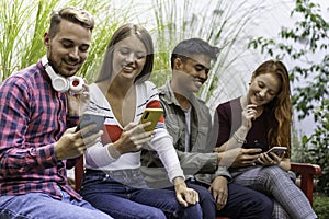 Multicultural friends having fun together looking at their smartphones  at dehor garden on college campus - People addicted by