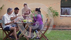 Multicultural friends laughing with big smile around the table. Woman serves the food at house patio. Smiles