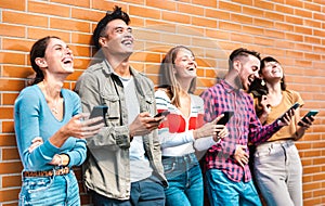 Multicultural friends laughing using smartphone at wall on university college campus - Young people addicted by mobile phone