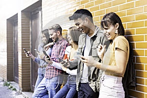 Multicultural friends laughing using smartphone at wall on university college campus - Young people addicted by mobile smart