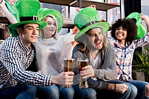 multicultural friends watching tv and clinking glasses saint patrick