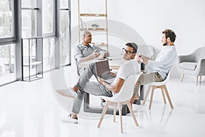 multicultural group of businessmen sitting at workplace in light