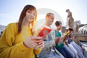 Multicultural group of smiling friends using mobile phones outdoors. People and technology addiction