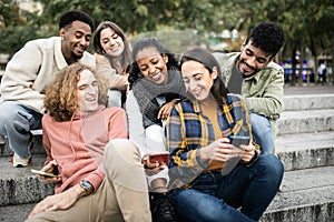 Multicultural group of young trendy friends using mobile phone in city street