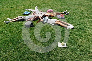 Multicultural schoolkids lying on lawn and covering faces with books