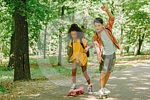 Multicultural schoolkids riding skateboards in green sunny park