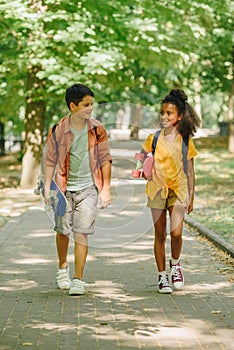 Multicultural schoolkids walking in park while holding skateboards