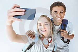 multicultural smiling teenagers taking selfie together on smartphone