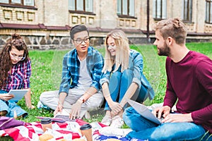 multicultural students with digital devices coffee to go and american flag resting on green