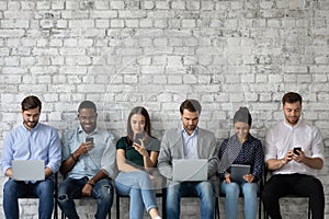 Multicultural team of gadget users sitting in line, using laptops