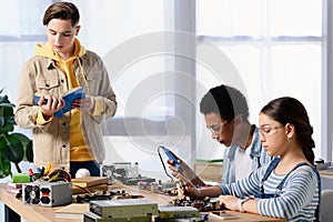 multicultural teenagers soldering computer circuit with soldering iron and friend