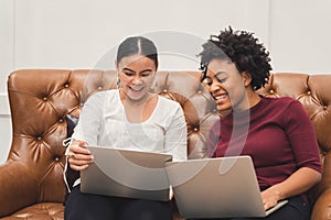 Multicultural women using a laptop on couch relaxing on the living room